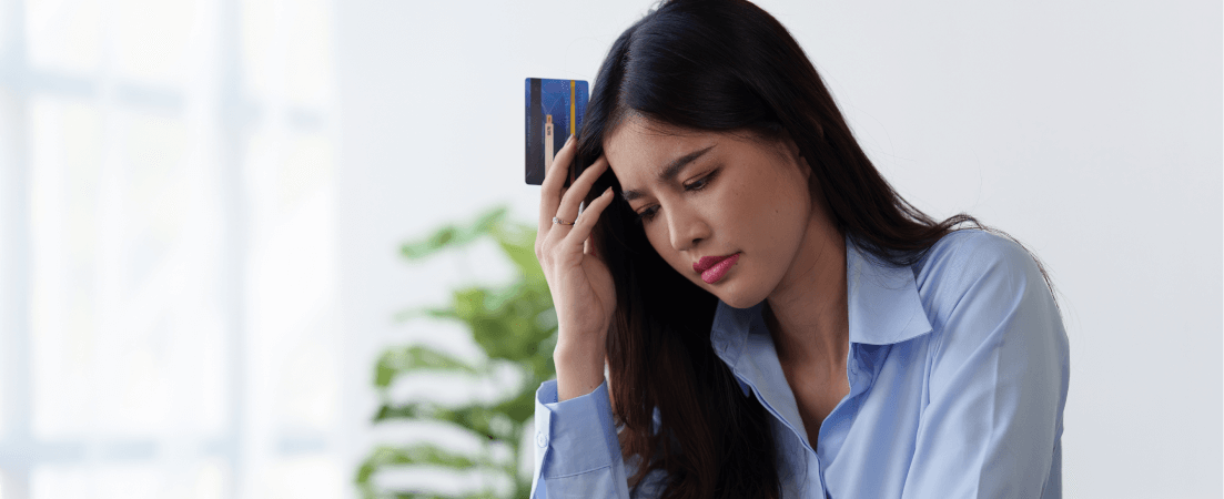 A worried woman holding a credit card is touching her head