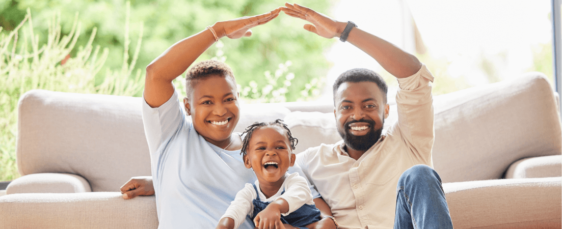Mother and father hold their arms up to form a house. Daughter sits on laps smiling