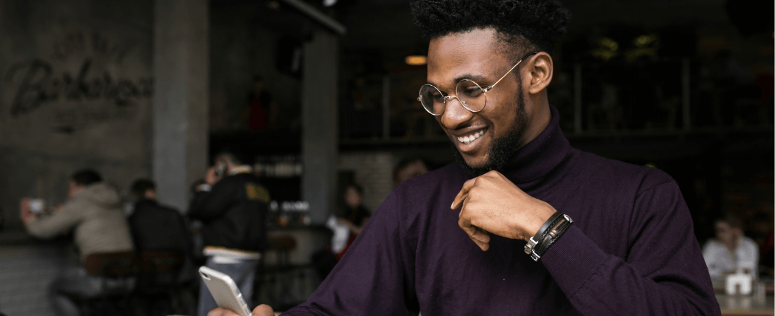 A young man with glasses smiles at his phone