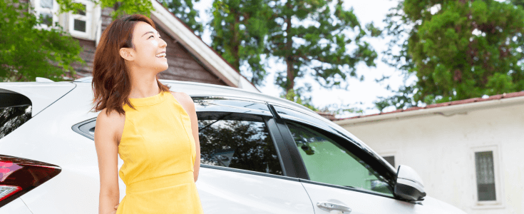 A woman stands in front of her car