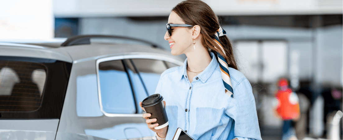 woman walking by car with coffee